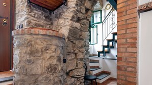 Un muro de piedra, una puerta de madera, una escalera con paredes blancas y detalles verdes, y una silla negra.