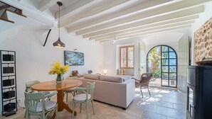 A spacious living area with a wooden dining table, green chairs, a beige sofa, and a large arched window.
