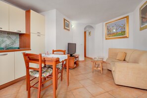 Un espacio habitable compacto con kitchenette, una mesa de comedor con sillas, un sofá y un televisor.