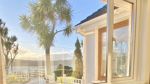 A room with a view of palm trees and a body of water. - Seaview Cottage on the Island (Islandmagee)