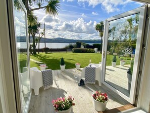 A balcony with a view of a lake, a grassy lawn, and a wooden deck. - Seaview Cottage on the Island (Islandmagee)