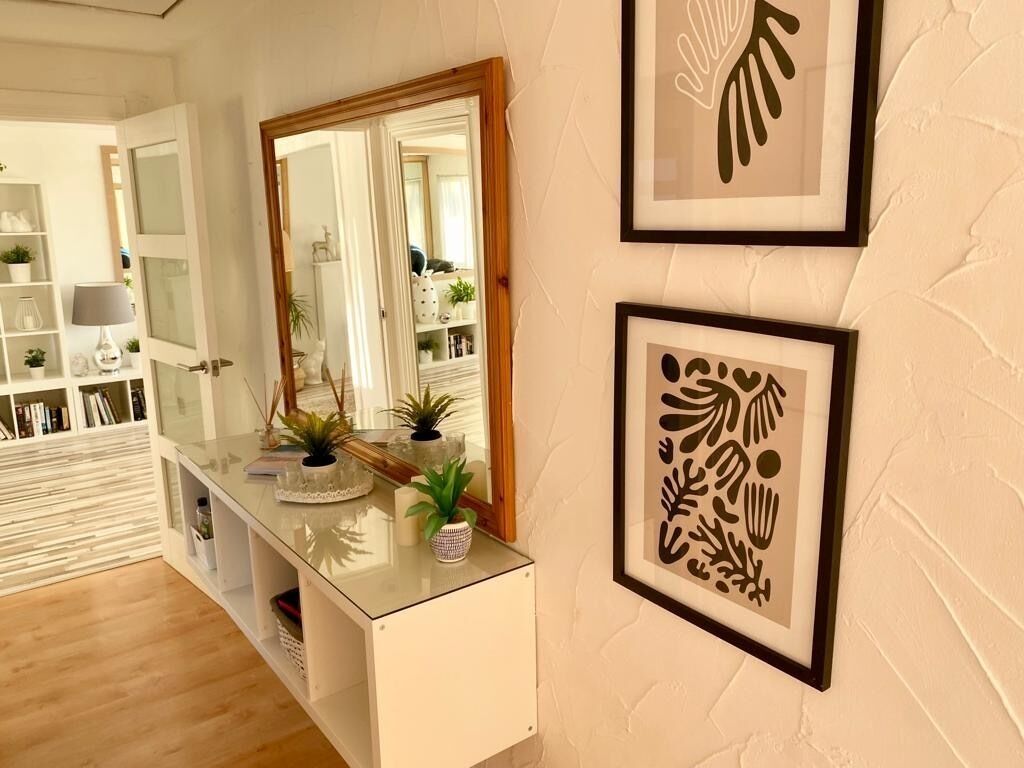 Una habitación con una consola blanca, un espejo y dos impresiones botánicas enmarcadas en la pared.
