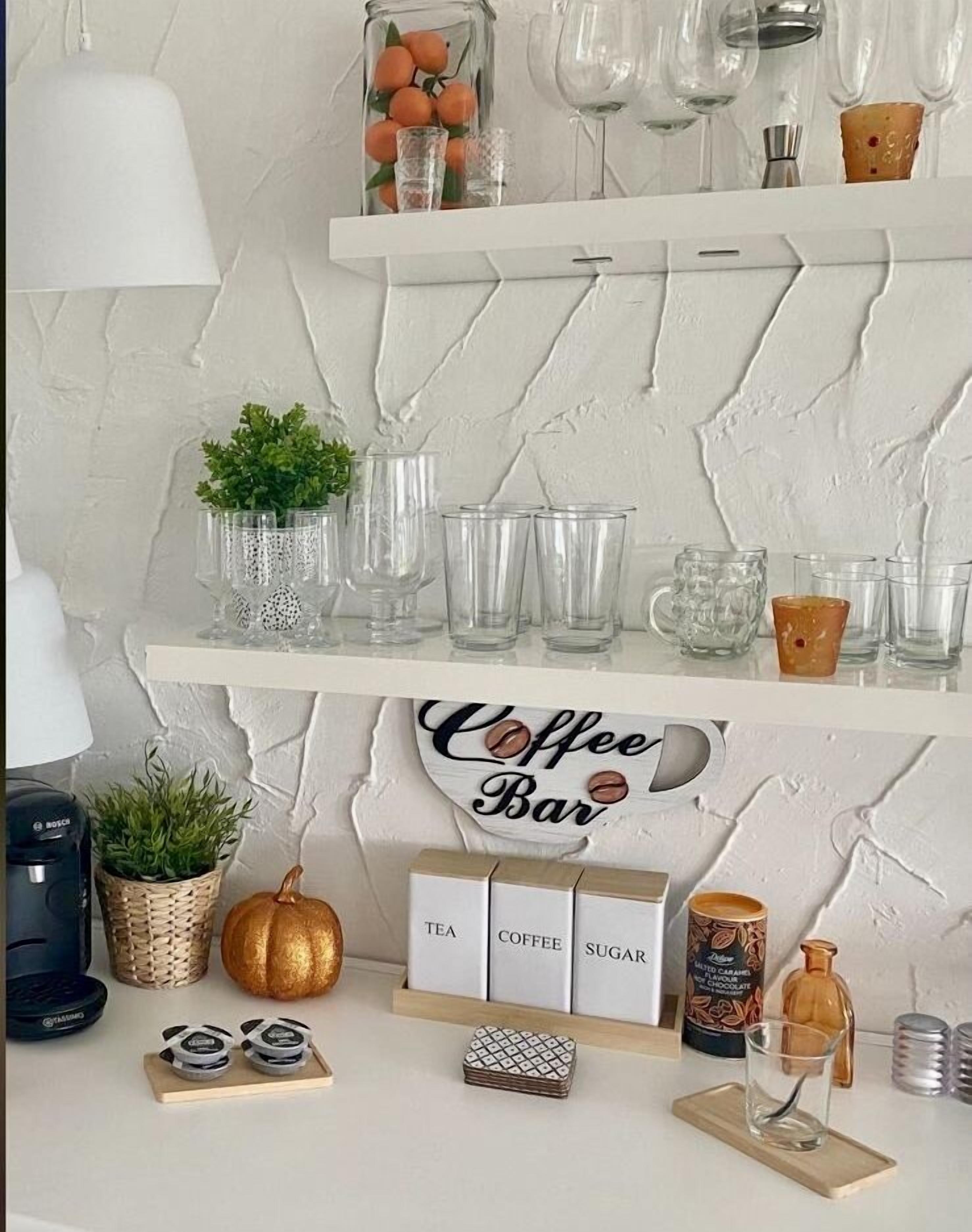 Um balcão de café com prateleiras exibindo copos, uma máquina de café e uma placa com a inscrição 'Coffee Bar'.
