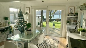 A modern kitchen with a glass dining table, white chairs, a Christmas tree, and a view of a lake through large sliding doors. - Seaview Cottage on the Island (Islandmagee)