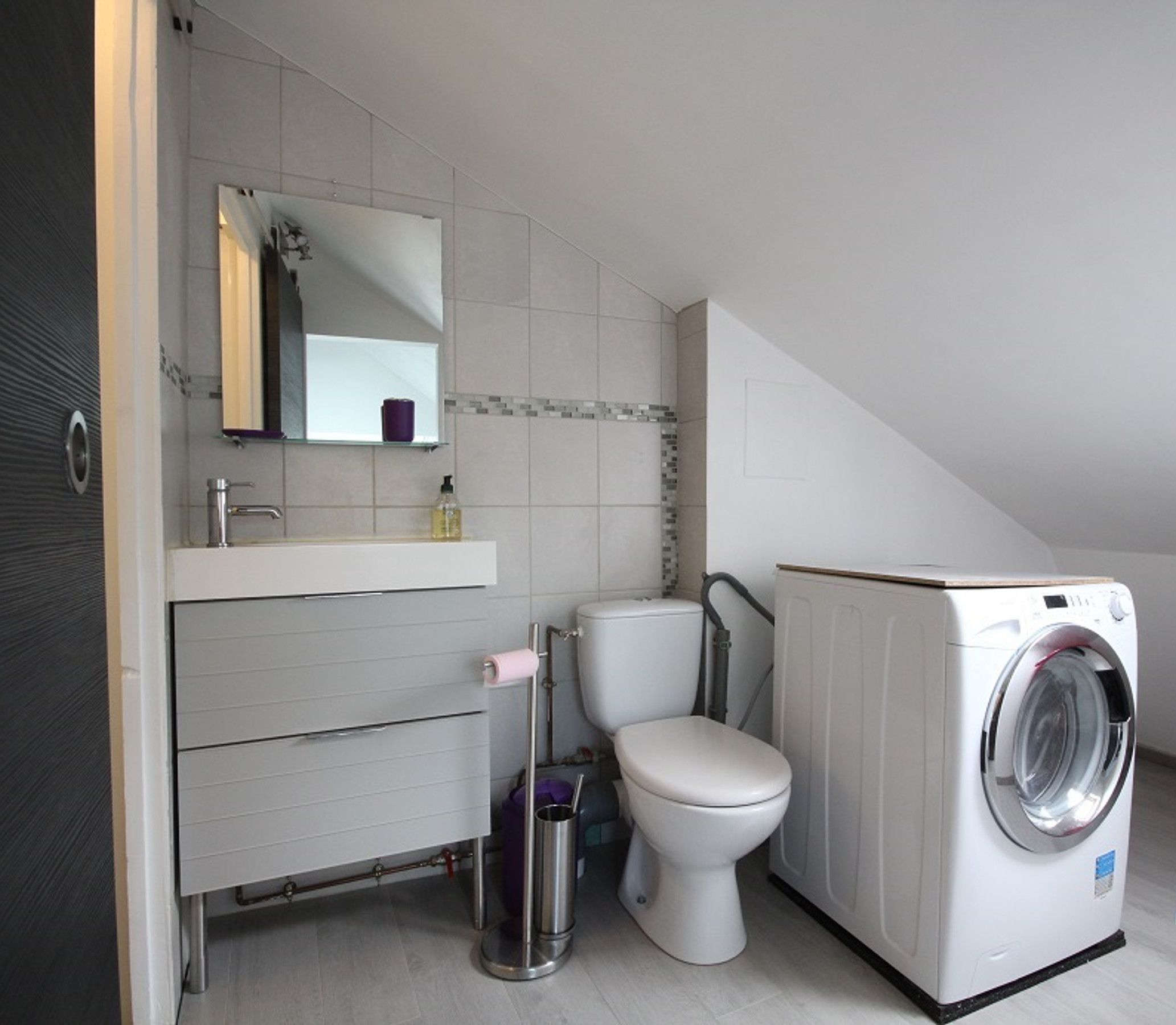 A compact, modern bathroom with a toilet, sink, and washing machine.