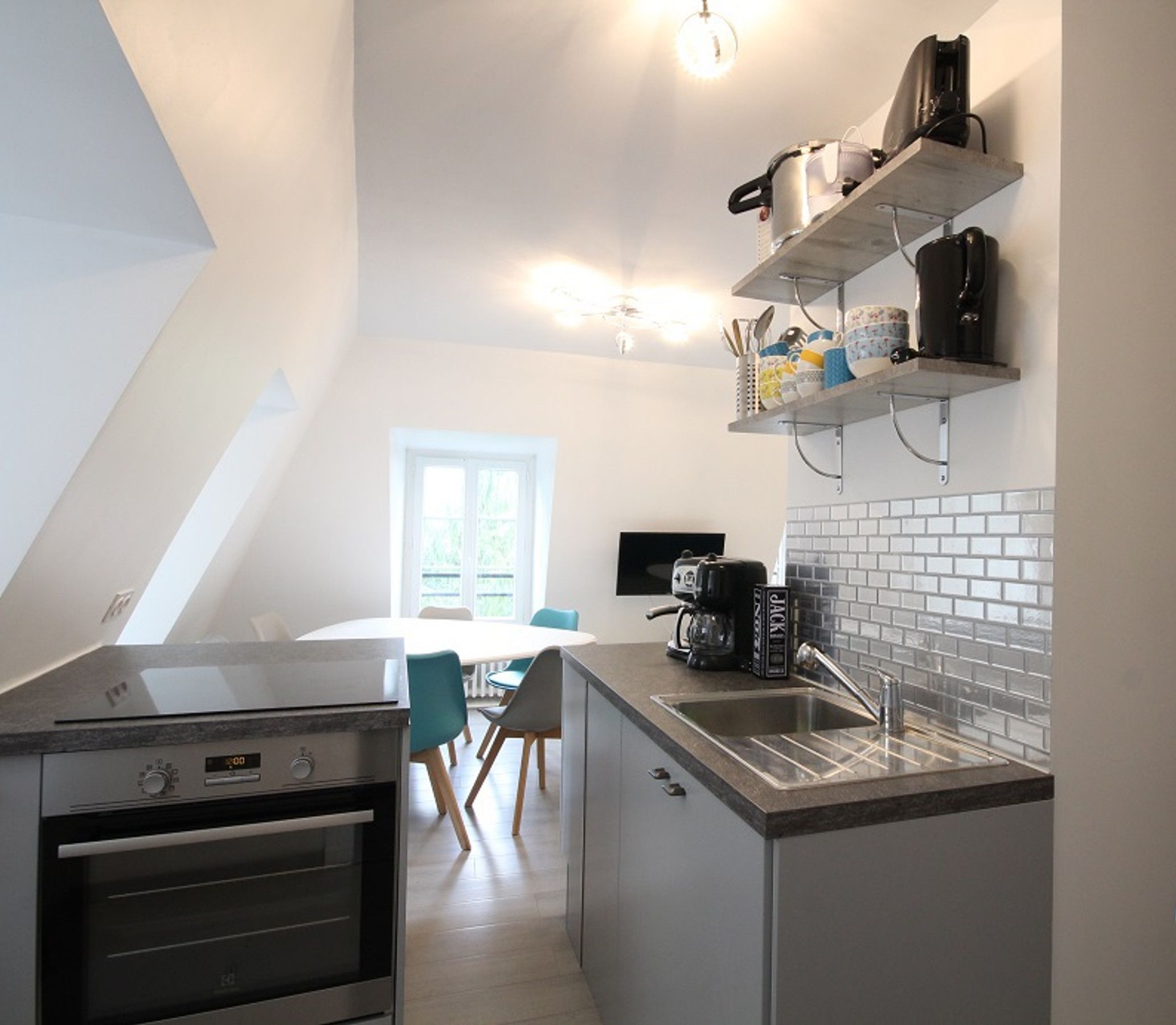 Eine moderne Küche mit Einbauofen, Kaffeemaschine und Spüle. Ein Essbereich mit Tisch und Stühlen ist ebenfalls vorhanden.