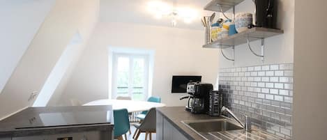 Eine moderne Küche mit Einbauofen, Kaffeemaschine und Spüle. Ein Essbereich mit Tisch und Stühlen ist ebenfalls vorhanden.