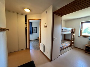 A compact room with a bunk bed, a radiator, a small window, and a door leading to another room.