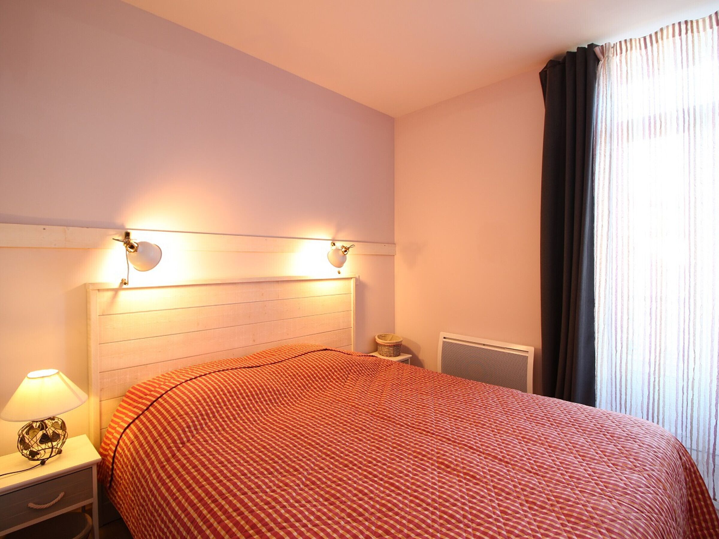 A neatly made bed with a checkered bedspread, a bedside lamp, and a nightstand with a lamp.