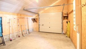 A spacious garage with a large white garage door, wooden walls, and a concrete floor. - Mont-Dore: 4-bedroom chalet with garage and terrace (Mont-Dore)