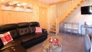 A cozy living room with a black leather sofa, a glass coffee table, and a wooden staircase. - Mont-Dore: 4-bedroom chalet with garage and terrace (Mont-Dore)