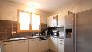 A modern kitchen with stainless steel appliances, a dishwasher, and a refrigerator. There is a window with curtains and a sink with a faucet. - Mont-Dore: 4-bedroom chalet with garage and terrace (Mont-Dore)