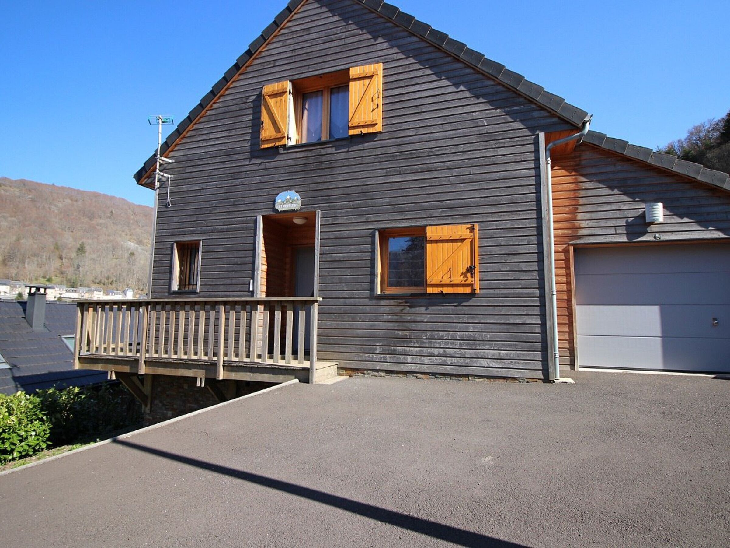 A two-story wooden building with a balcony, a garage, and a small window with shutters.