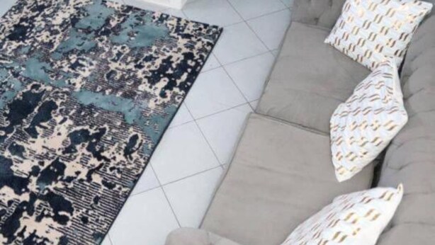 Ein Wohnzimmer mit grauem Sofa, einem gemusterten Teppich und einem weißen Couchtisch.