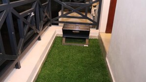 Ein kleiner Außenbereich mit Kunstgras, einem Grill und einer Metallbank.