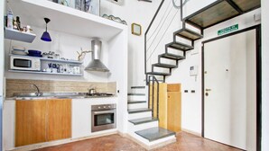 A modern kitchen with a built-in oven, microwave, and sink. There is a staircase leading to a door marked "USCITA DI EMERGENZA".