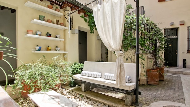 A cozy outdoor seating area with a cushioned bench, surrounded by potted plants and a stone pathway.