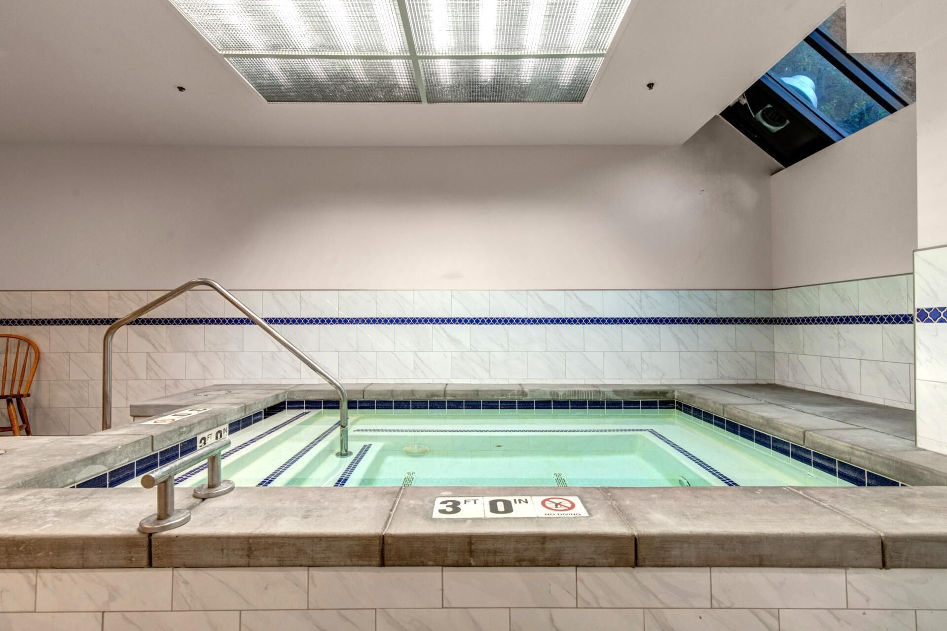 A spa pool with a 30 ft depth sign, tiled walls, and a skylight.