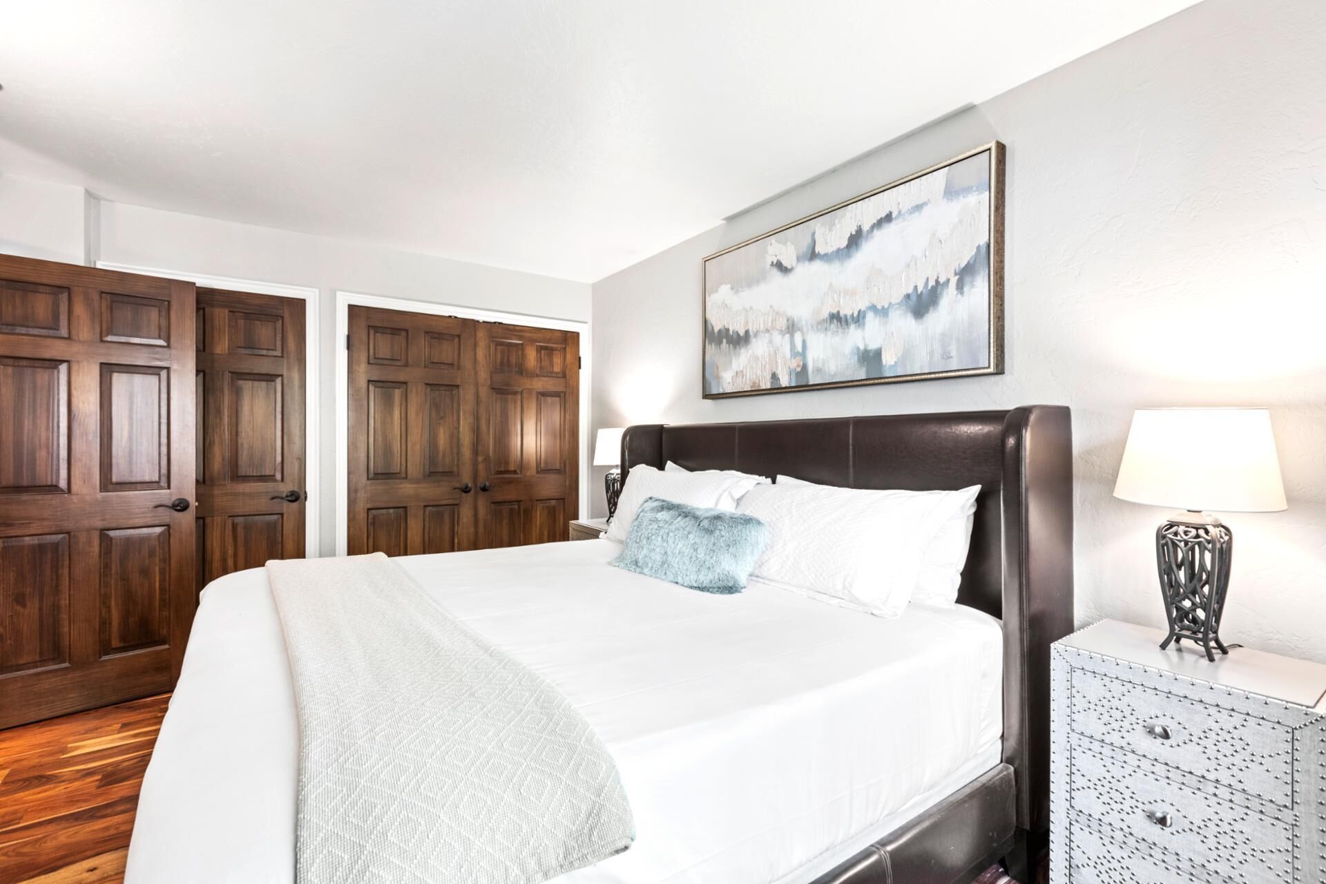 A bedroom with a large bed, a nightstand, a lamp, and two doors.