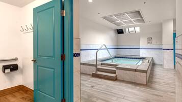 Una puerta azul verdosa que da a un baño con una bañera, un pasamanos y un letrero de emergencia 911 en la pared.