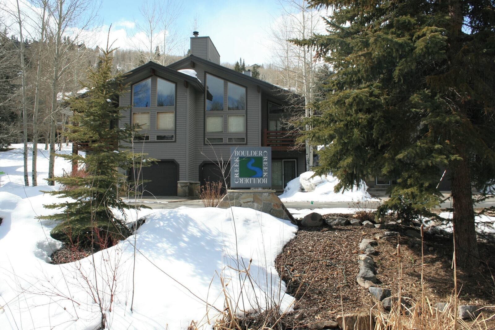 A modern two-story building with large windows, a stone foundation, and a sign indicating 'Boulder Creek.'
