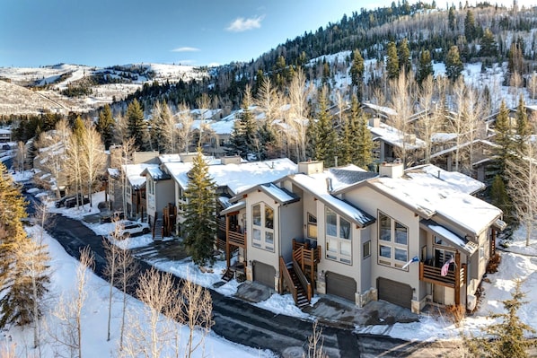 Un quartier résidentiel avec des maisons modernes, une route et un paysage enneigé, avec des arbres et des collines en arrière-plan.