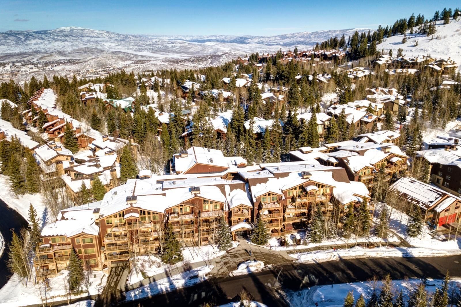 A snow-covered resort with multiple buildings, a ski slope, and a mountainous backdrop.