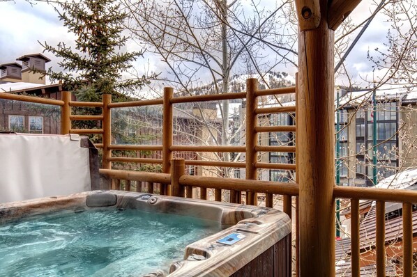 Un jacuzzi con valla de madera, un árbol y un edificio al fondo.