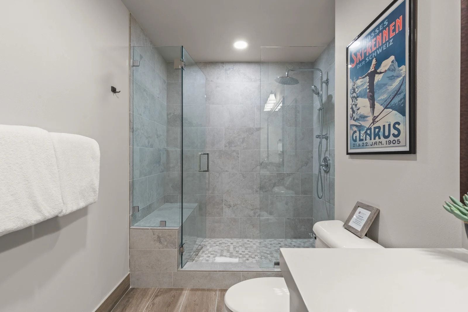 A modern bathroom with a glass-enclosed shower, a white toilet, and a framed poster on the wall.