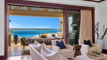 Une pièce avec vue sur l’océan, un coin repas avec du mobilier d’extérieur, et un espace détente avec des canapés blancs et une table basse.