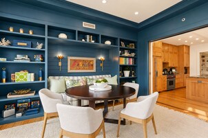 Una sala de estar moderna con una pared de acento azul oscuro, una mesa de comedor redonda y una cocina visible a través de un vano abierto.