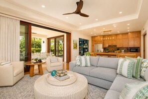 A modern living room with a sofa, a coffee table, and a dining area with wooden cabinets and a kitchen in the background.