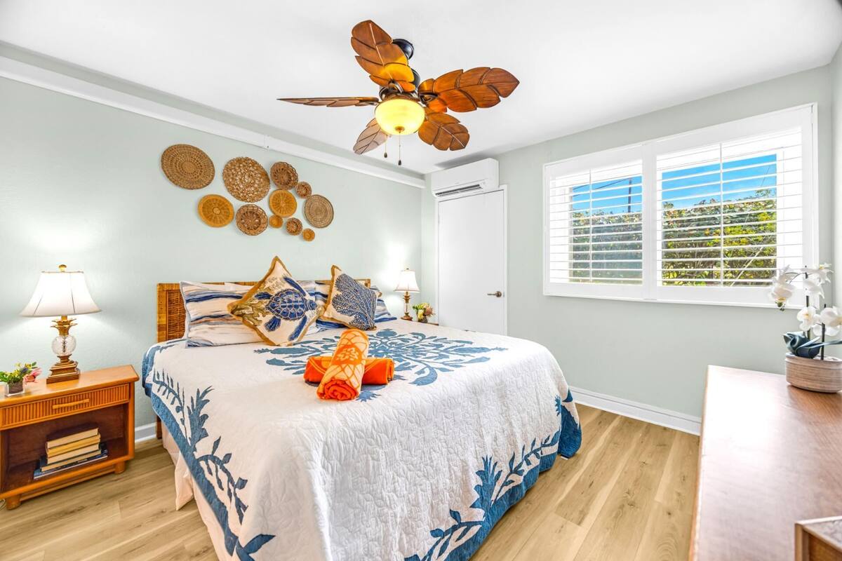 A bedroom with a bed, a ceiling fan, a window with blinds, and decorative wall art.