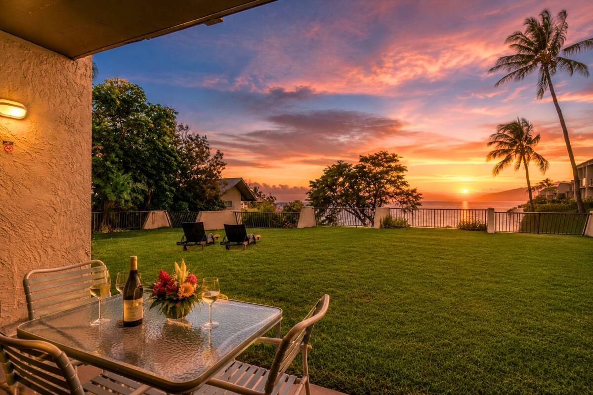A patio with a table set for two, a bottle of wine, and a vase of flowers.