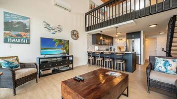 A spacious living area with a large TV, a wooden coffee table, and a kitchen with bar stools.