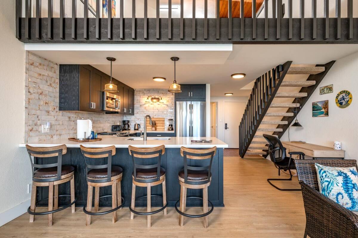 A modern kitchen with a central island, bar stools, and a staircase leading to an upper level.