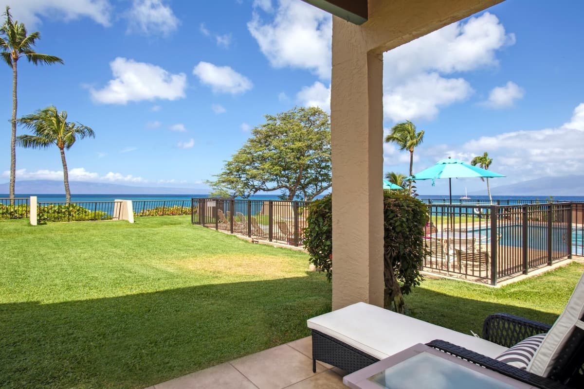 A patio with a pool, lounge chairs, and a view of the ocean.