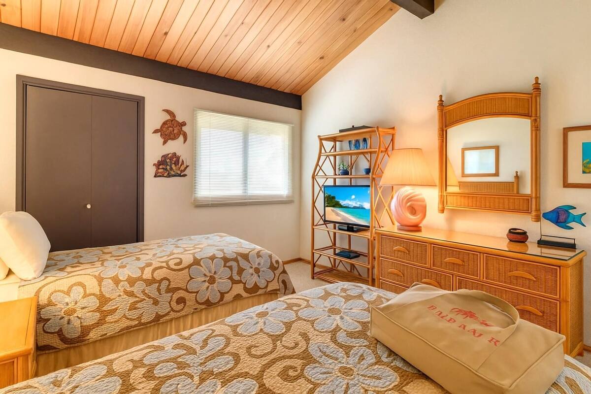 A bedroom with two beds, a wooden dresser, a TV, and a window with blinds.