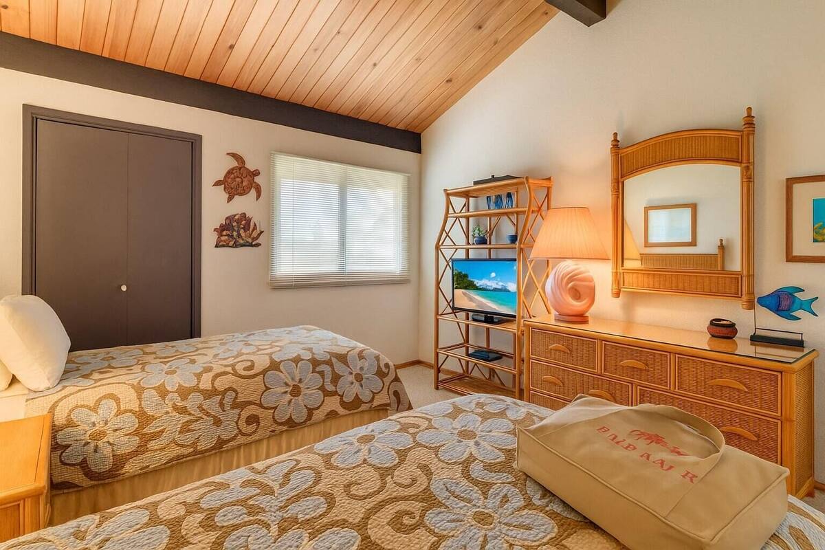 A room with two beds, a TV, a dresser, and a window with blinds.