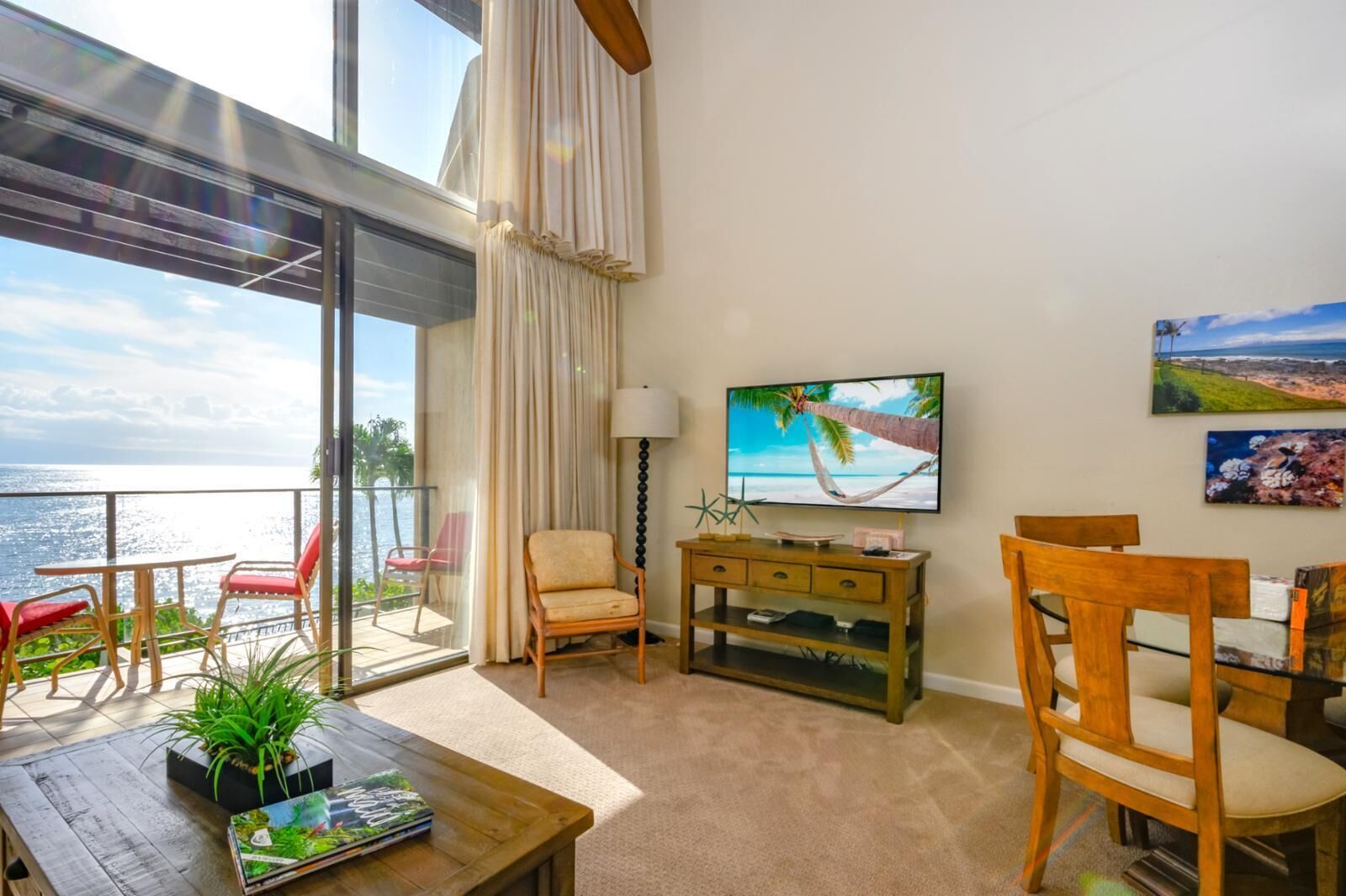 Un balcón con vista al mar, un televisor y un comedor con sillas y una mesa.