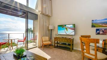 Un balcón con vista al mar, un televisor y un comedor con sillas y una mesa.