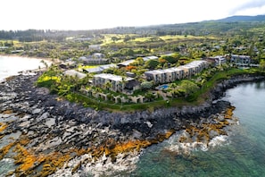 An aerial view of a coastal resort with multiple buildings, a rocky shoreline, and clear waters. - Napili Point Resort by KBM (Napili-Honokowai)
