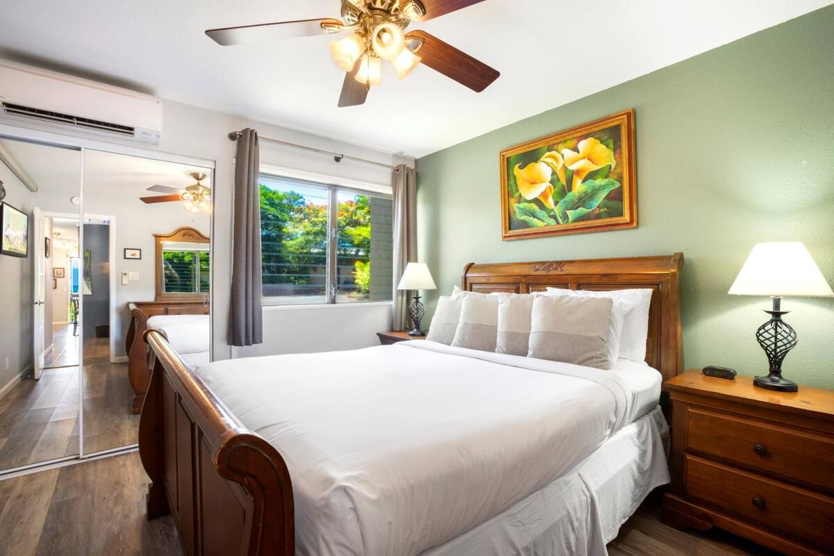 A hotel room with a large bed, two bedside tables, a ceiling fan, and a window with curtains.