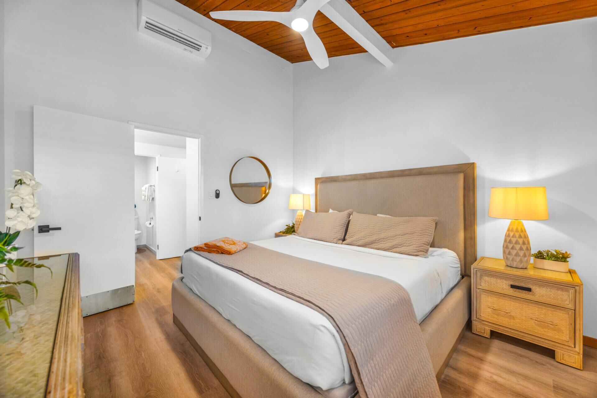 A bedroom with a large bed, bedside lamps, a mirror, and a wooden ceiling.