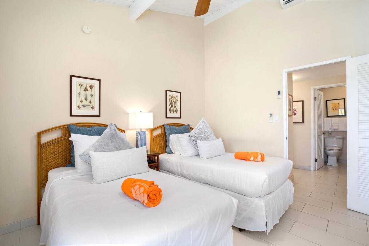 A hotel room with two beds, a bathroom, and a hallway.