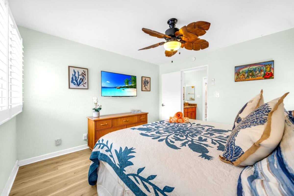 A bedroom with a bed, a ceiling fan, a TV, and artwork on the walls.