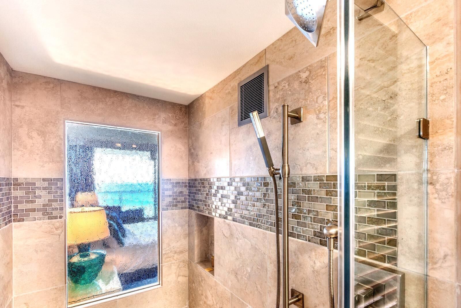 A modern shower with a glass enclosure, a tiled backsplash, and a visible vent.