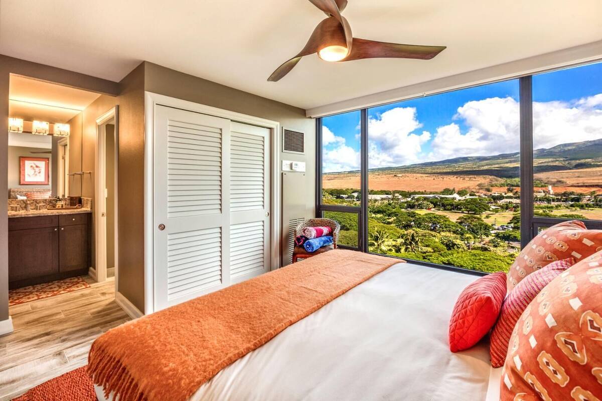 A bedroom with a large window, a ceiling fan, and a view of a landscape.