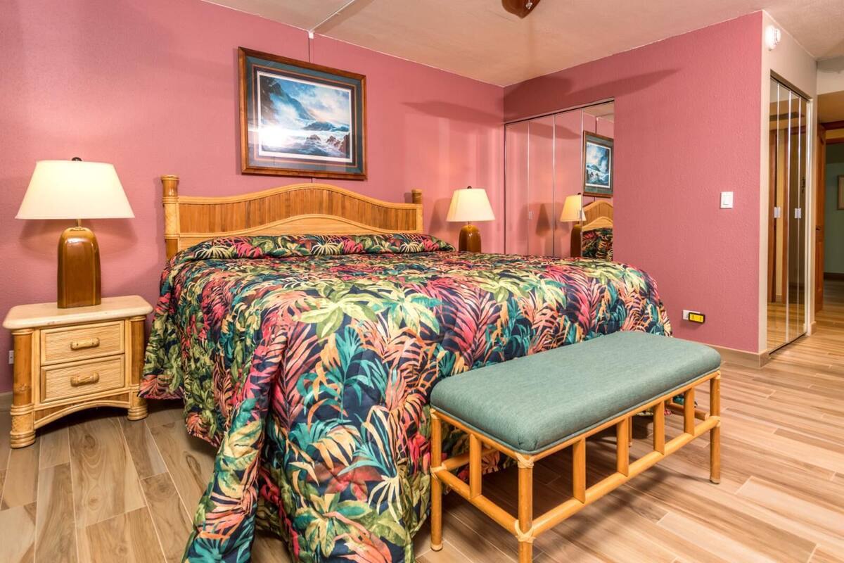 A bedroom with a bed, two bedside tables with lamps, a bench, a large mirror, and a framed picture on the wall.