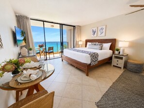 A hotel room with a bed, a dining table with chairs, a balcony with a view of the sea, and a TV mounted on the wall. - Mahana Resort by KBM (Kaanapali)